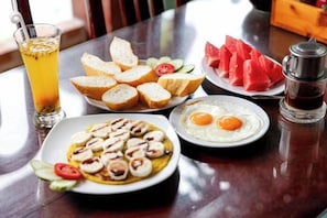 Une table en bois dressée pour le petit-déjeuner, avec des toasts, des œufs et des tranches de pastèque.
