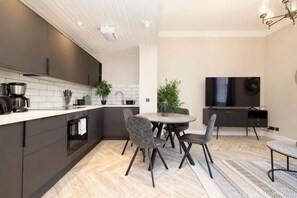 Une cuisine moderne avec des meubles de couleur sombre, un plan de travail blanc et un coin repas comprenant une table ronde et des chaises.