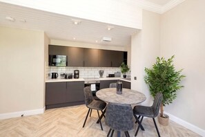 Une cuisine moderne avec des meubles de couleur sombre, une table de salle à manger ronde entourée de chaises et une plante en pot.