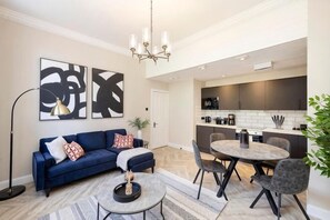 Un salon moderne avec un canapé bleu, une table basse ronde et un coin repas comprenant une table ronde et des chaises.