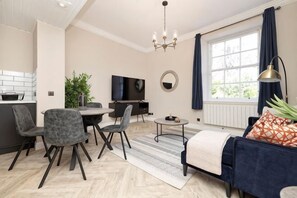 En moderne stue med sofa, stole, et fjernsyn, et spisebord og et køkkenområde.