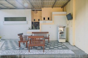 Un espace extérieur abrité avec des sièges, un sol à carreaux, un banc en bois et un réfrigérateur.