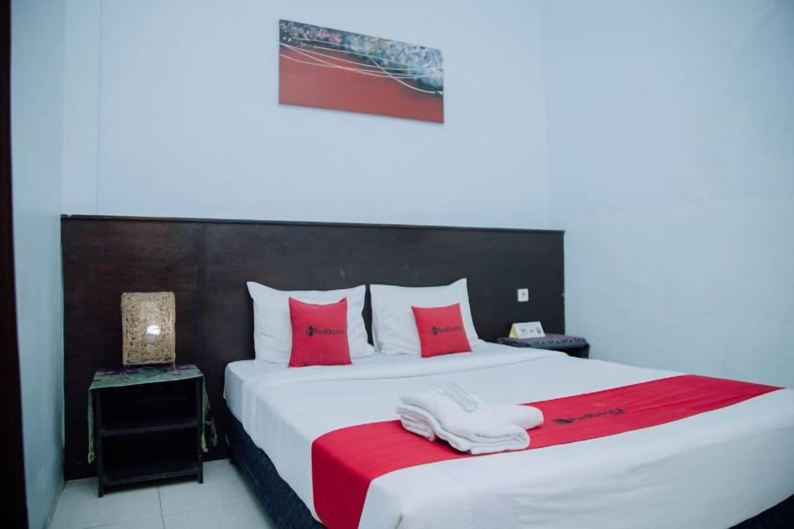 A hotel room with a bed, a nightstand, a lamp, and a painting on the wall.