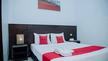 A hotel room with a bed, a nightstand, a lamp, and a painting on the wall.