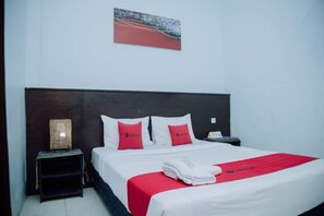 A hotel room with a bed, a nightstand, a lamp, and a painting on the wall. - RedDoorz @ Hening Homestay (Gunung Sari)