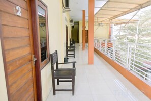 A corridor with wooden doors, a bench, and a balcony with a railing. - RedDoorz @ Hening Homestay (Gunung Sari)