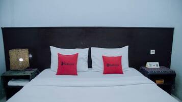 A bed with white sheets, two red pillows, a dark headboard, and a small table with a lamp on the side.