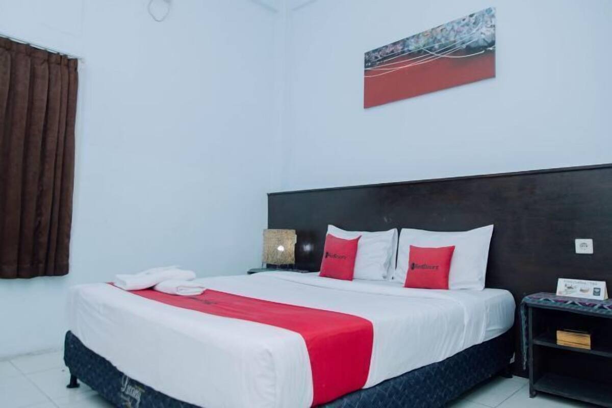 A hotel room with a bed, a nightstand, a wall-mounted artwork, and a window with curtains.