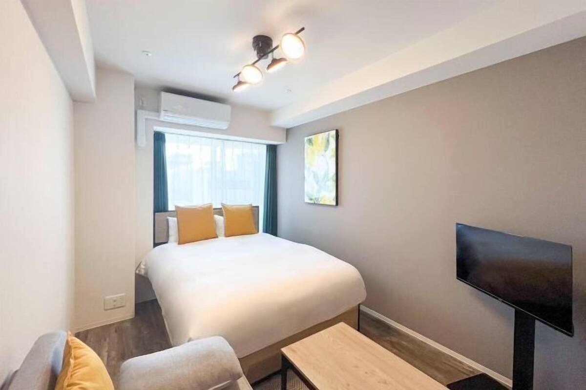 Una habitación de hotel moderna con una cama grande, un televisor de pantalla plana, una mesita y una ventana con cortinas.