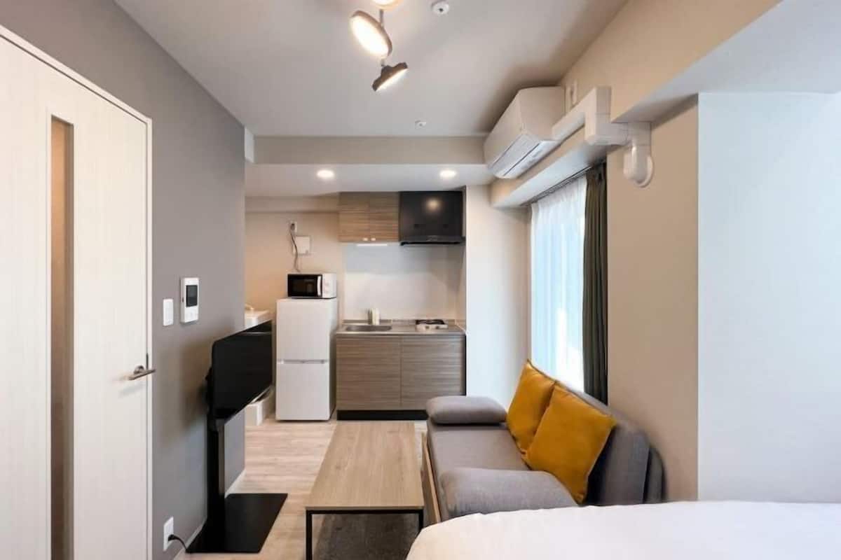 Habitación compacta y moderna con kitchenette, un sofá con un cojín color mostaza y una cama.