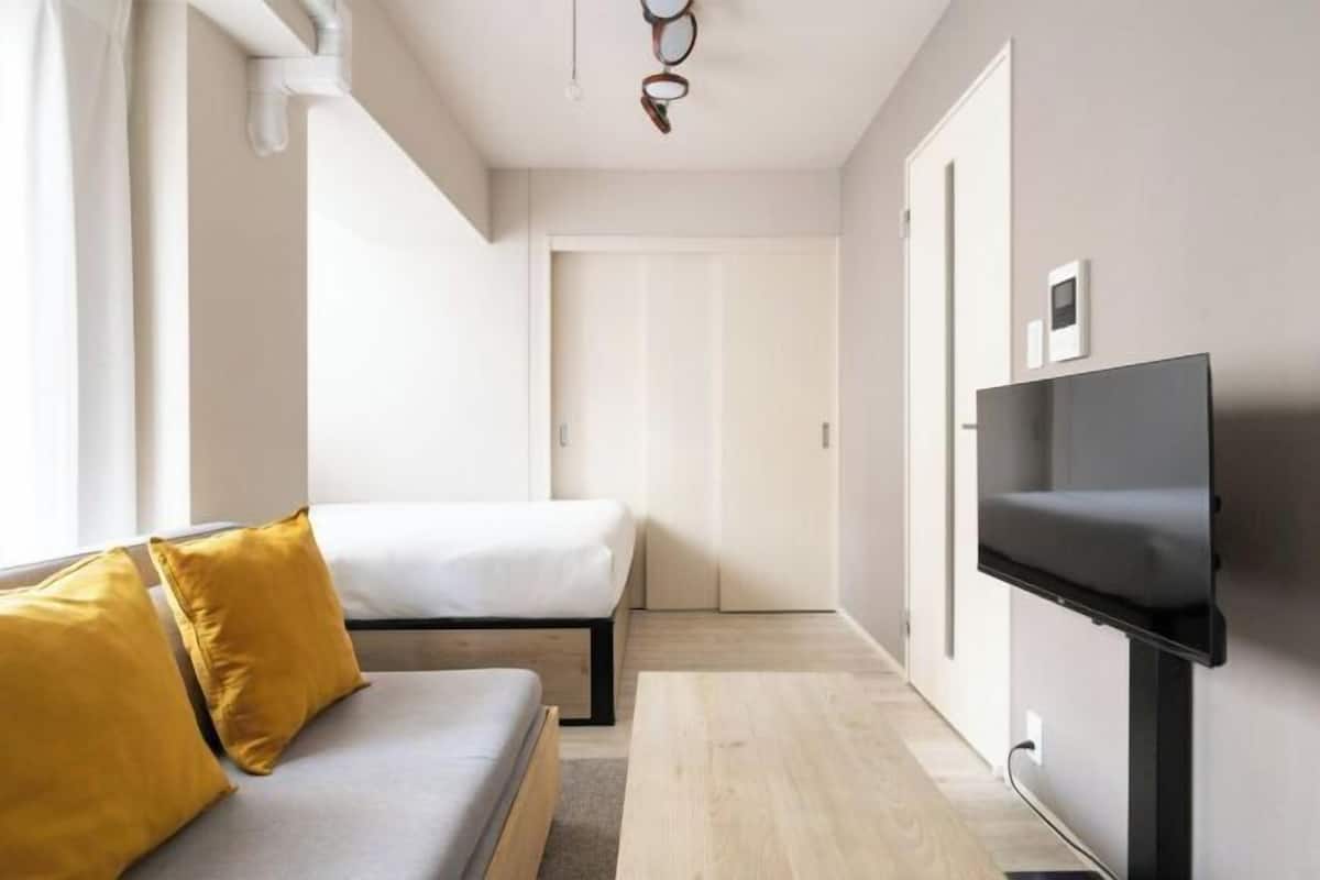 A modern hotel room with a sofa, a bed, a flat-screen TV mounted on the wall, and a wooden floor.