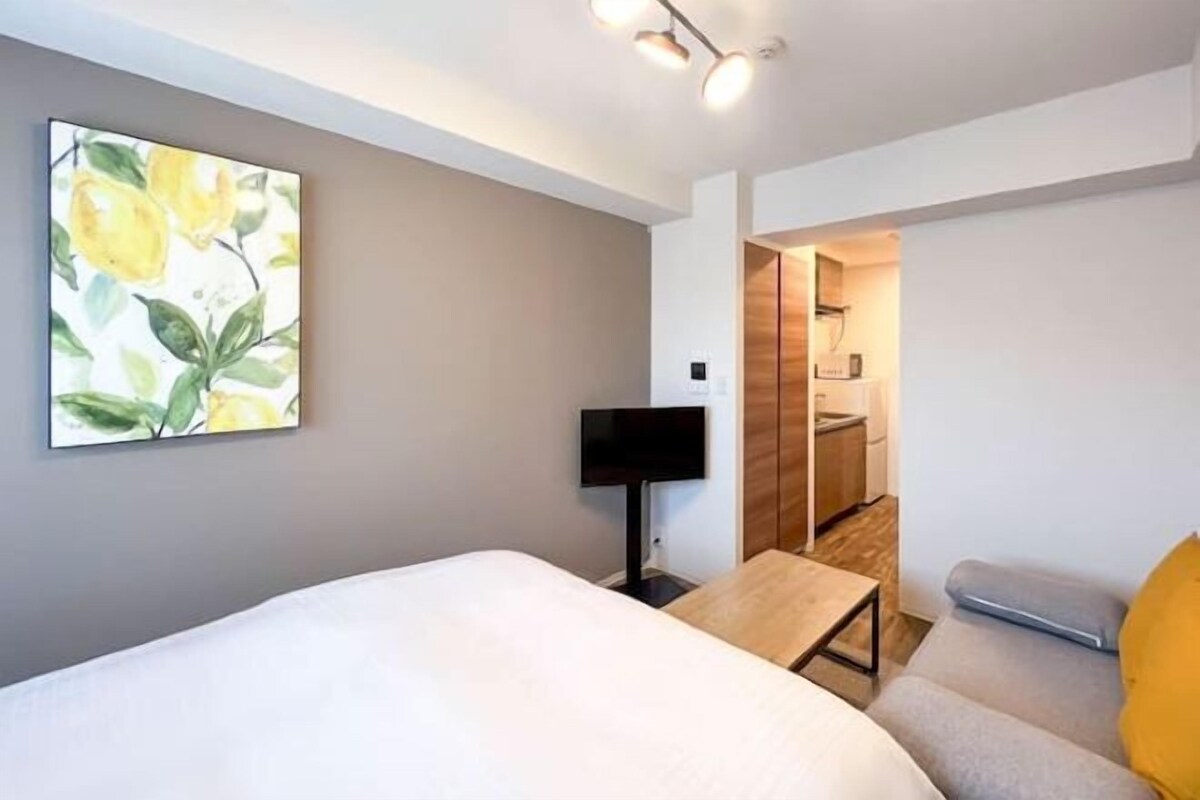 A hotel room with a bed, a bedside table, a TV, and a painting on the wall.