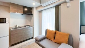A modern kitchen with a built-in oven, microwave, and sink. There's a sofa with cushions and a wooden coffee table. - LAFESTA Higashi Komagata　 (Tokyo)