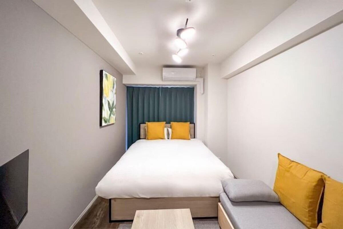 A modern hotel room with a bed, a sofa, a flat-screen TV, and a ceiling light fixture.