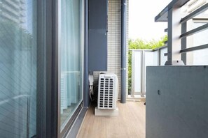 A narrow outdoor corridor with a glass door, a white air conditioning unit, and a grey wall. - LAFESTA Higashi Komagata (Tokyo)