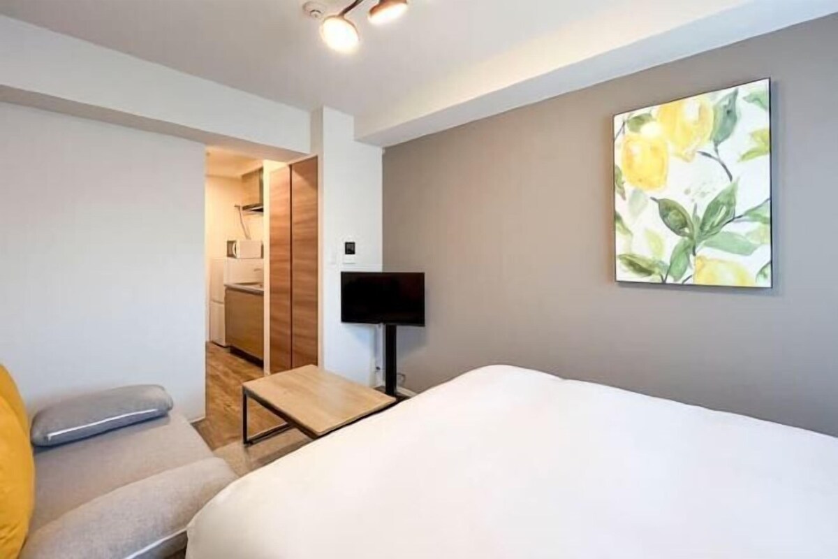 A modern hotel room with a bed, a small desk, a TV, and a painting on the wall.