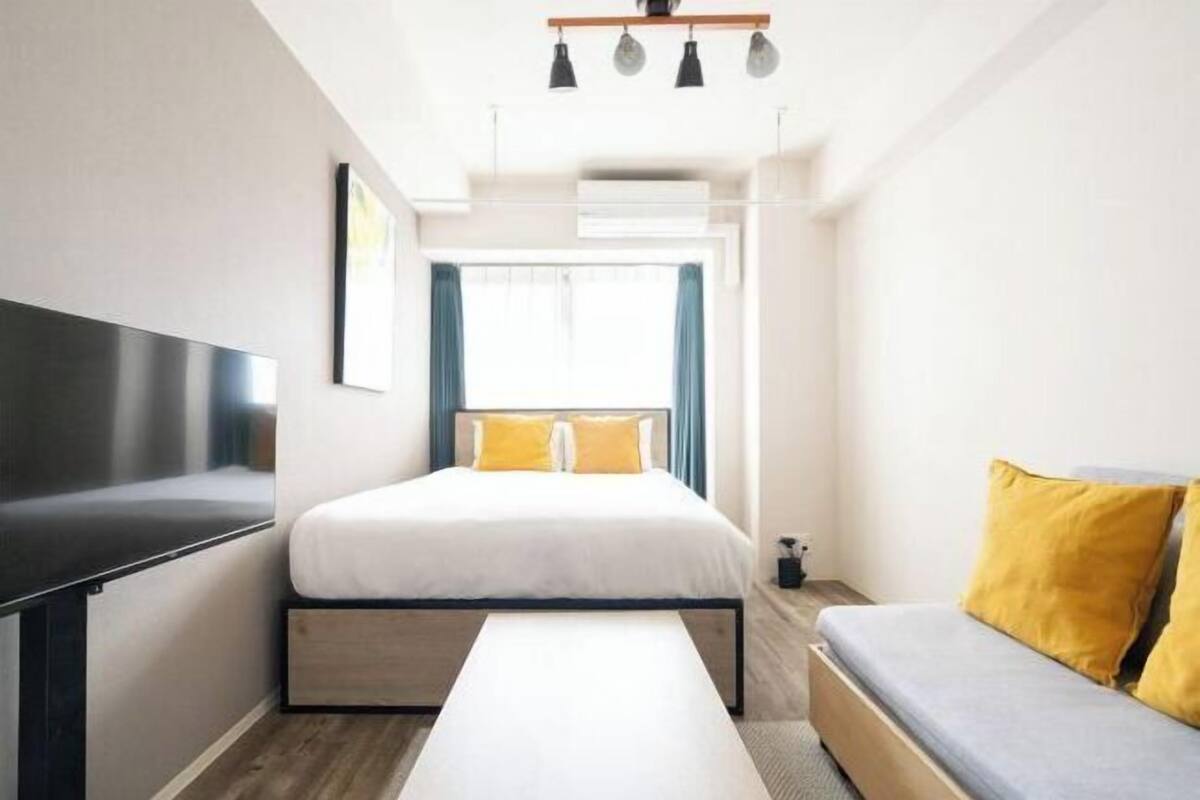 Una habitación de hotel moderna con una cama, un sofá, un televisor de pantalla plana y un ventanal con cortinas.