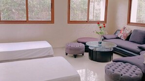 A room with a bed, a sofa, two ottomans, a coffee table, and large windows with a view of trees. - Morocco Casablanca Polar Bear Airport Homestay (Nouaceur)