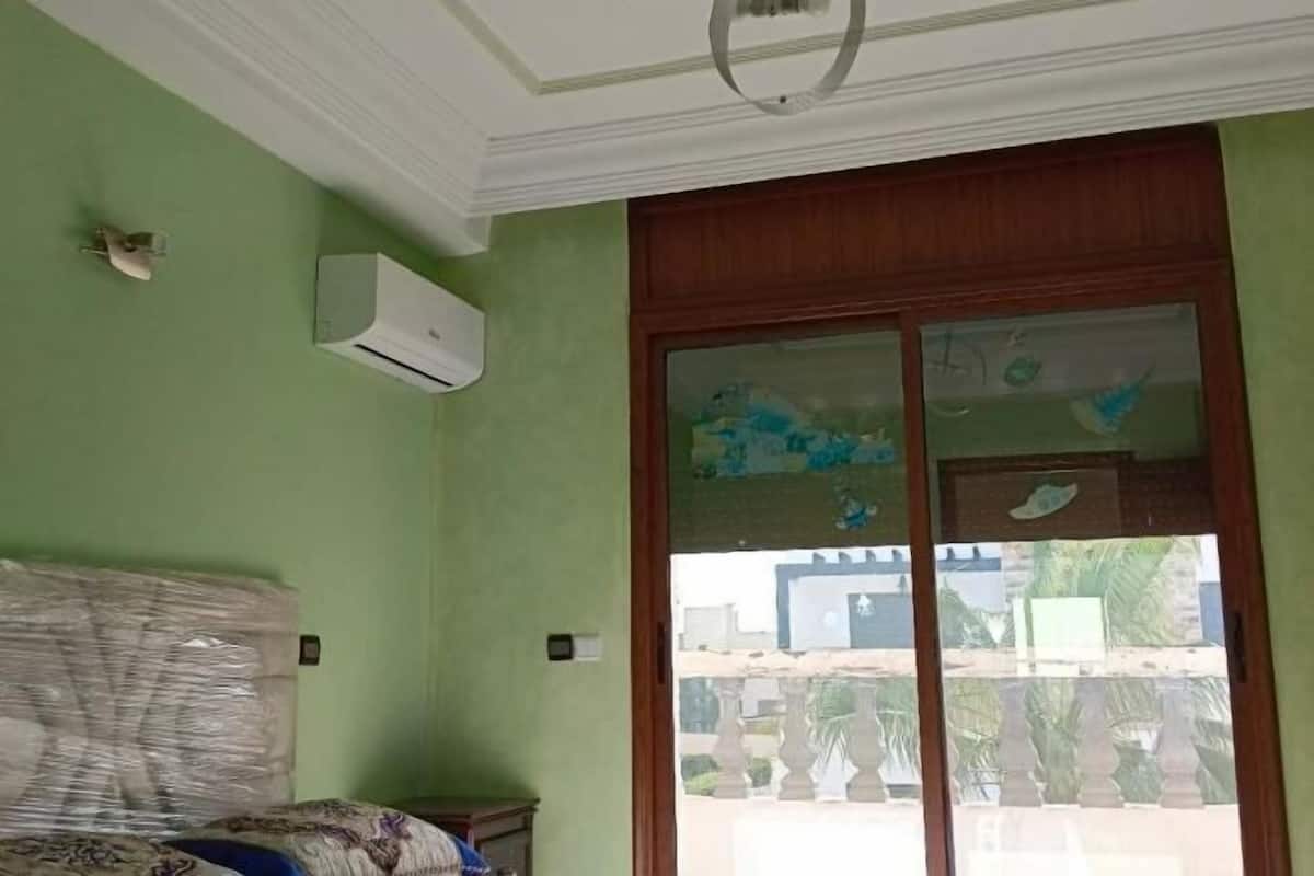 A room with green walls, a wooden door with glass panels, and an air conditioning unit mounted on the wall.