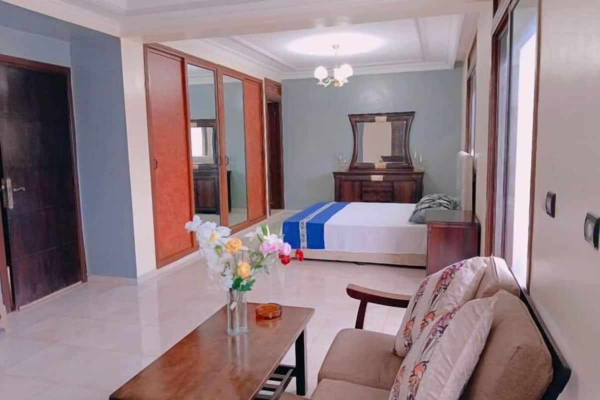 A hotel room with a bed, a desk with a vase of flowers, a chair, and a mirror on the wall.