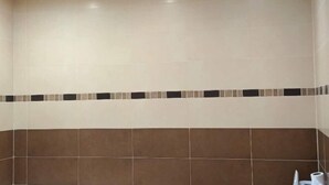 A bathroom with beige and brown tiles, a decorative border, and a toilet paper holder. - Morocco Casablanca Polar Bear Airport Homestay (Nouaceur)