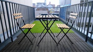 Ein Balkon mit Tisch und Stühlen, eine kleine Rasenfläche und Blick auf die Stadt.