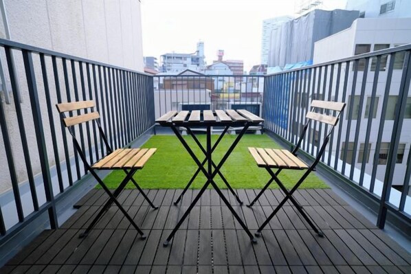 Un balcon avec une table et des chaises, un petit coin d’herbe et une vue sur la ville.