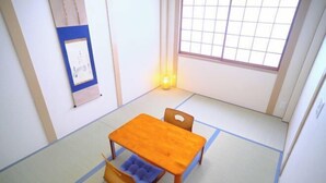 Ein Raum mit Tatami-Matten, einem Holztisch, Stühlen, einem Shoji-Bildschirm und einer kleinen Lampe.