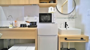 Eine kompakte Küche mit Mikrowelle, Kühlschrank, Spüle und einer kleinen Arbeitsplatte mit Wasserkocher und Tassen.