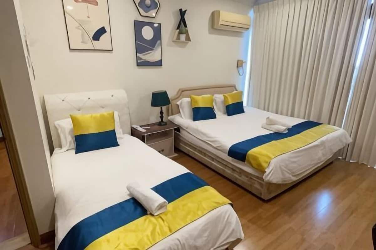 A hotel room with two beds, a nightstand, a lamp, and a window with curtains.