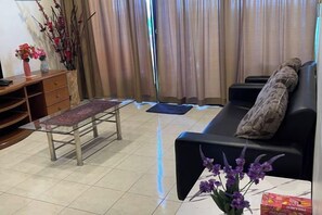 A living room with a sofa, a small table, a bench, and a TV stand. - Highfloor Riverbank Suites level 12 (Kuching)