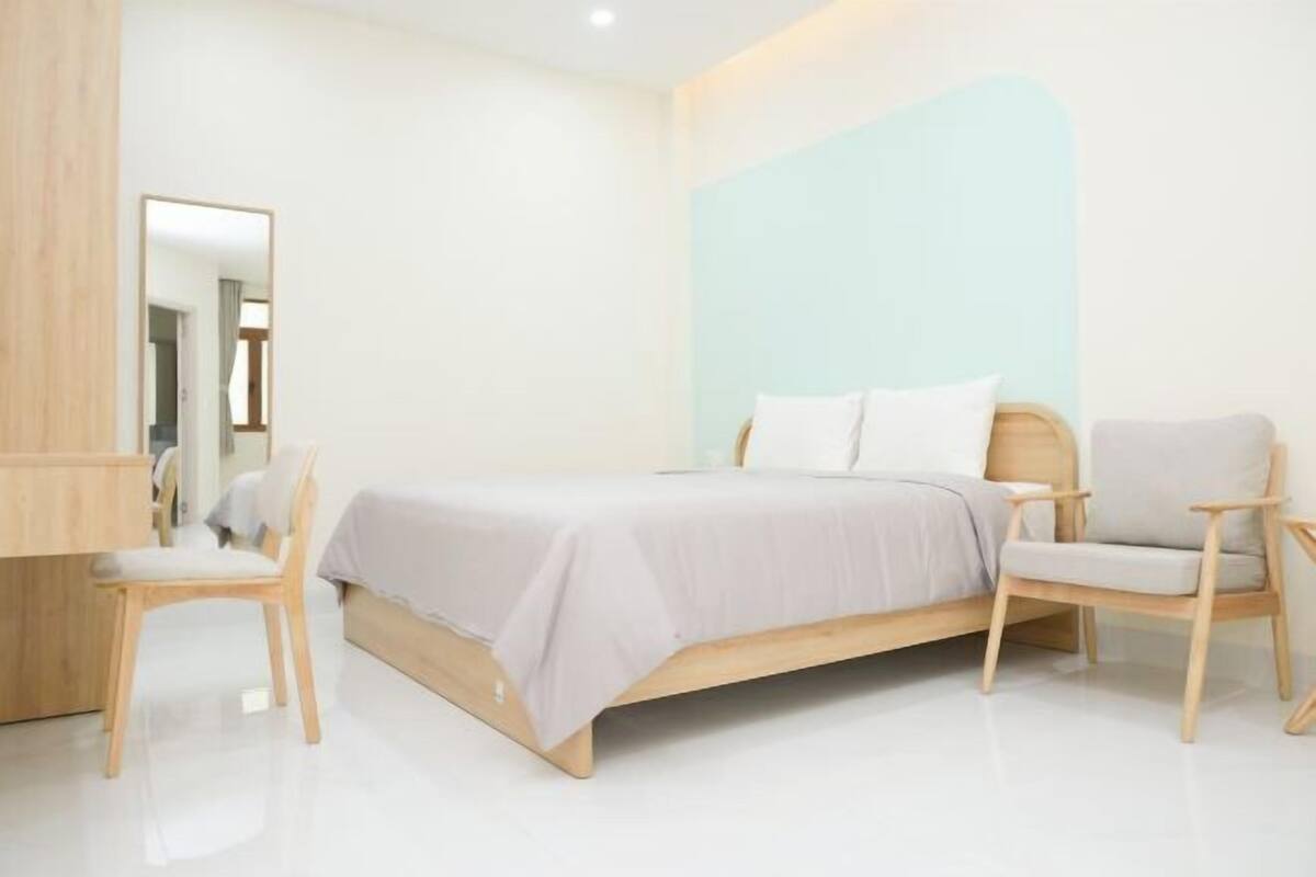 A modern bedroom with a bed, two chairs, a desk, and a mirror.