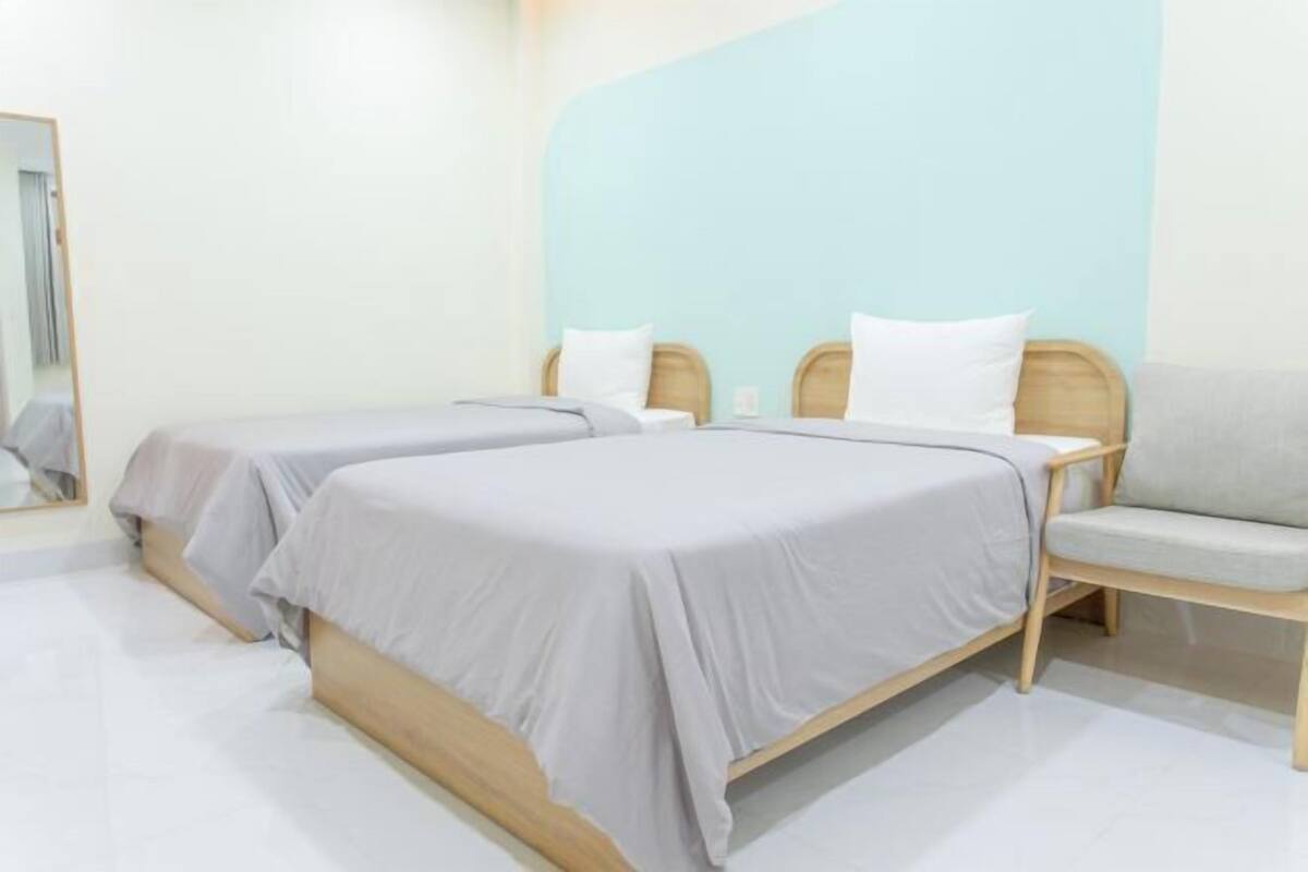 A room with two beds, a sofa, a mirror, and a light blue accent wall.