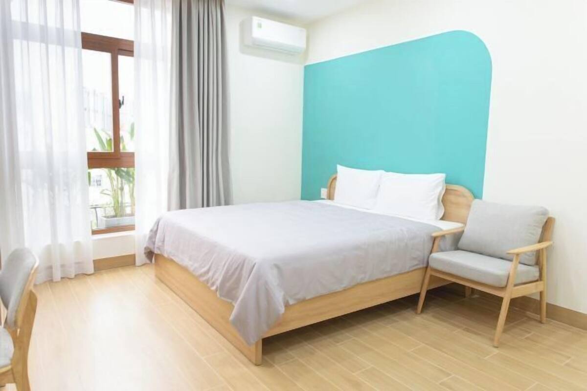 A bedroom with a bed, a chair, a window with curtains, and an air conditioning unit.