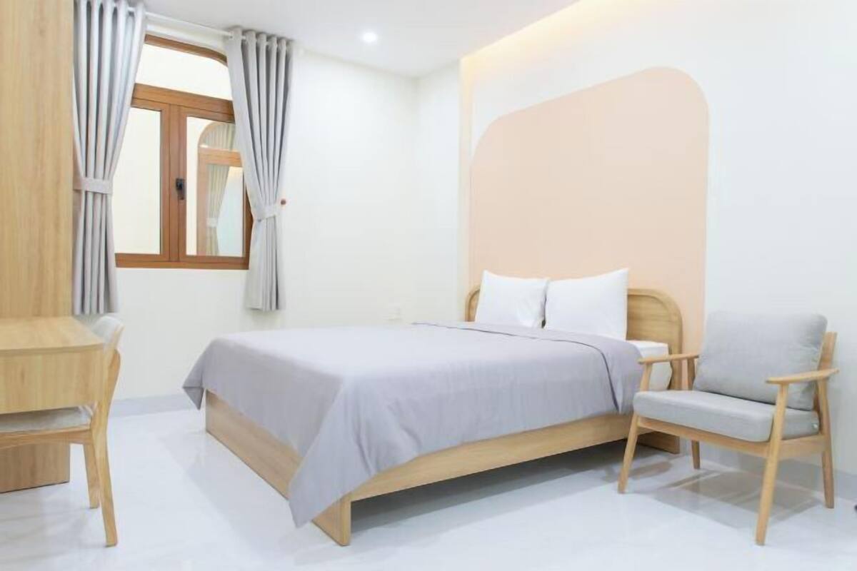 A bedroom with a bed, a chair, a desk, and a window with curtains.