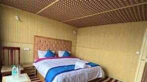 A hotel room with a large bed, a wooden nightstand, a chair, and a patterned carpet. - Alpine Cottage Pangong (Spangmik)