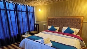 A hotel room with a large bed, a nightstand, and a window with curtains. - Alpine Cottage Pangong (Spangmik)