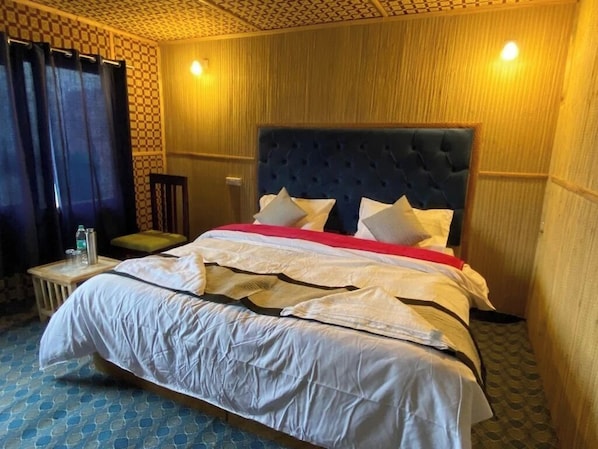 A neatly made bed with a tufted headboard, a bedside table with a bottle and glass, and a patterned floor. - Alpine Cottage Pangong (Spangmik)