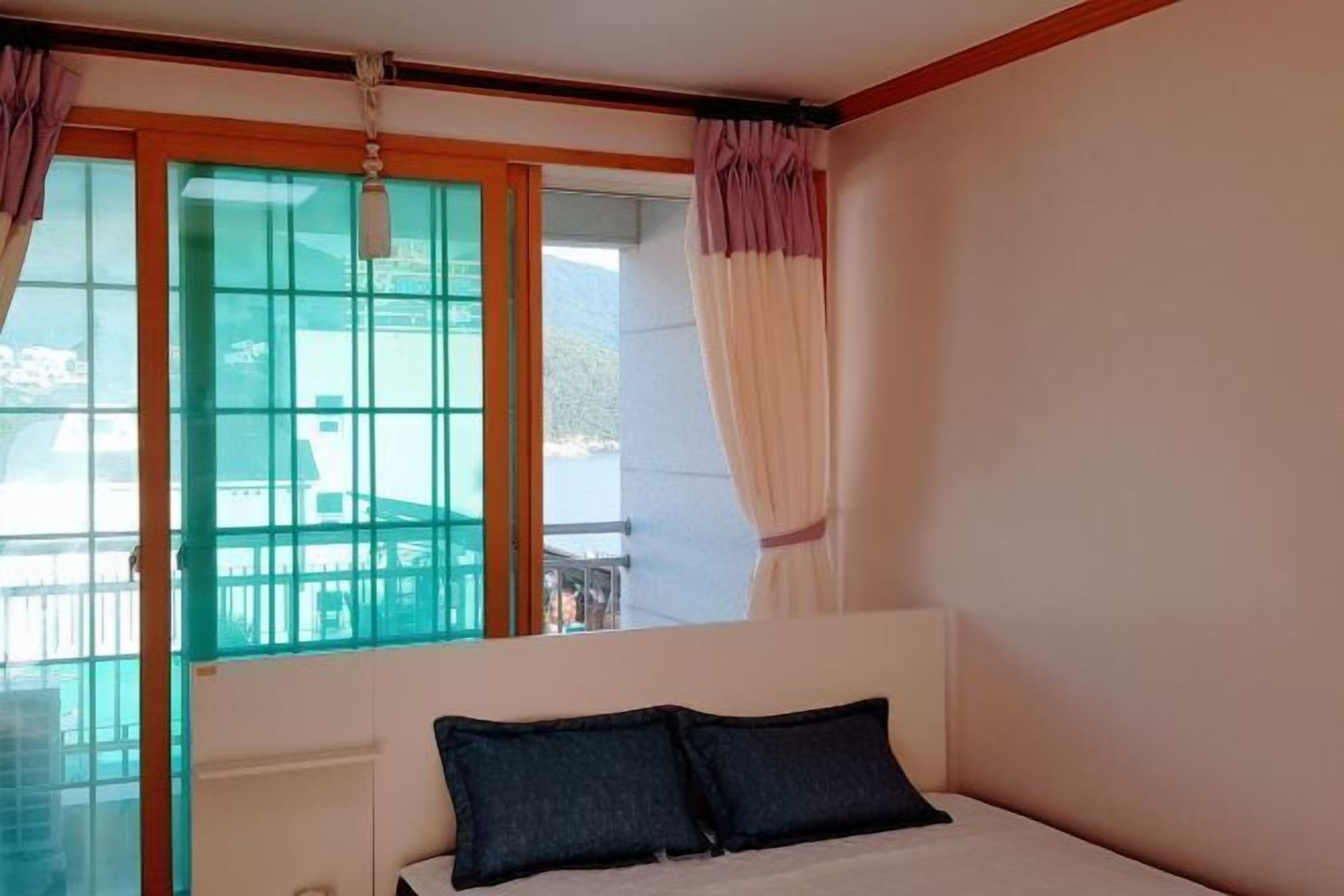 A bedroom with a bed, a window with curtains, and a view of a balcony.