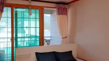A bedroom with a bed, a window with curtains, and a view of a balcony.