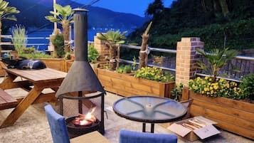 An outdoor seating area with a fire pit, tables, and chairs, surrounded by planters and a brick wall.