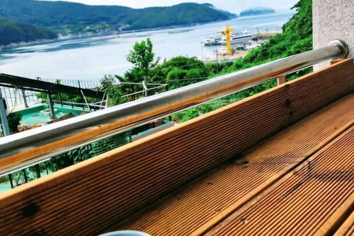 A wooden deck with a metal railing overlooking a river and industrial area.