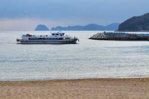 A ferry boat on calm water with a beach and distant mountains in the background. - Ha-Wahyeon HOUSE: Great location, views and vibe! (Geoje-si)