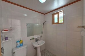 A bathroom with a toilet, sink, and shower. There are shelves with toiletries and a window. - Ha-Wahyeon HOUSE: Great location, views and vibe! (Geoje-si)