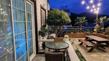 An outdoor patio with tables and chairs, a large window, and string lights.