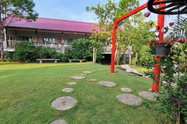A well-maintained lawn with stepping stones, a red metal structure, and a building with a red roof in the background.