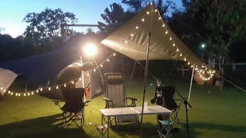 A tent with string lights, a table, and chairs set up on a grassy area.