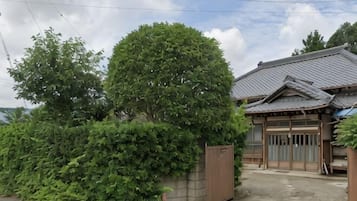 A traditional Japanese house with a tiled roof, a wooden gate, and a large tree in front.