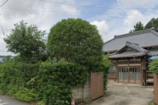 Una casa tradicional japonesa con techo de tejas, una puerta de madera y un gran árbol en primer plano.