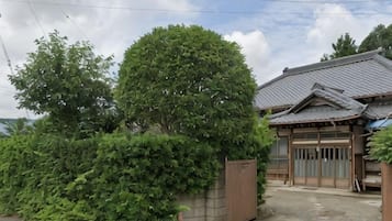 Una casa tradicional japonesa con techo de tejas, una puerta de madera y un gran árbol en primer plano.